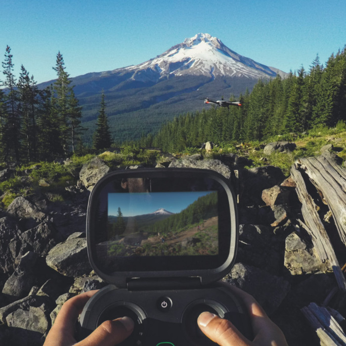 Drone flying with person holding controller with screen in view.